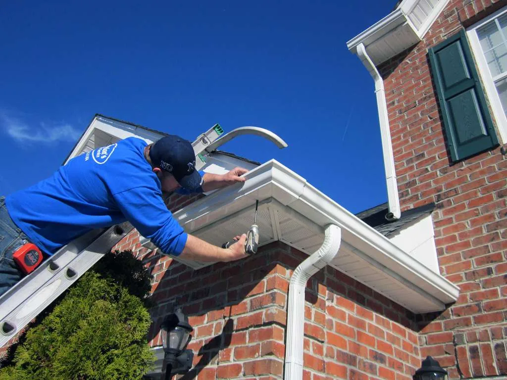 Installer fastening a new seamless metal gutter along the fascia of a residential roofline